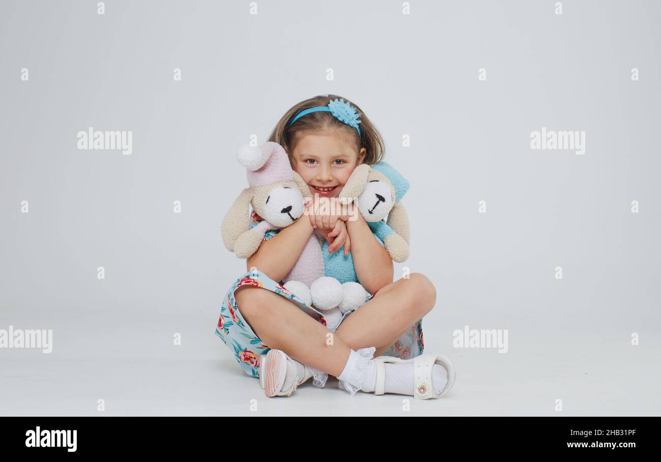 A little girl in a bright dress hugs two favorite toys on a white isolated background. Stock Photo