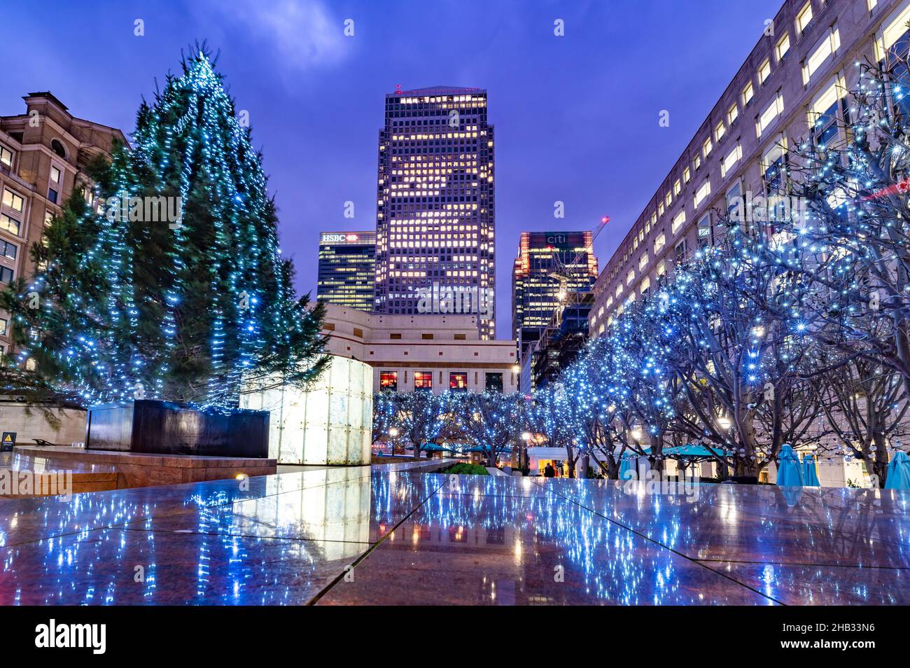 London, England, UK - December 15, 2021: Wide view of the Cabot and One Canada Square illuminated in evening lights, surrounded by Christmas tree deco Stock Photo