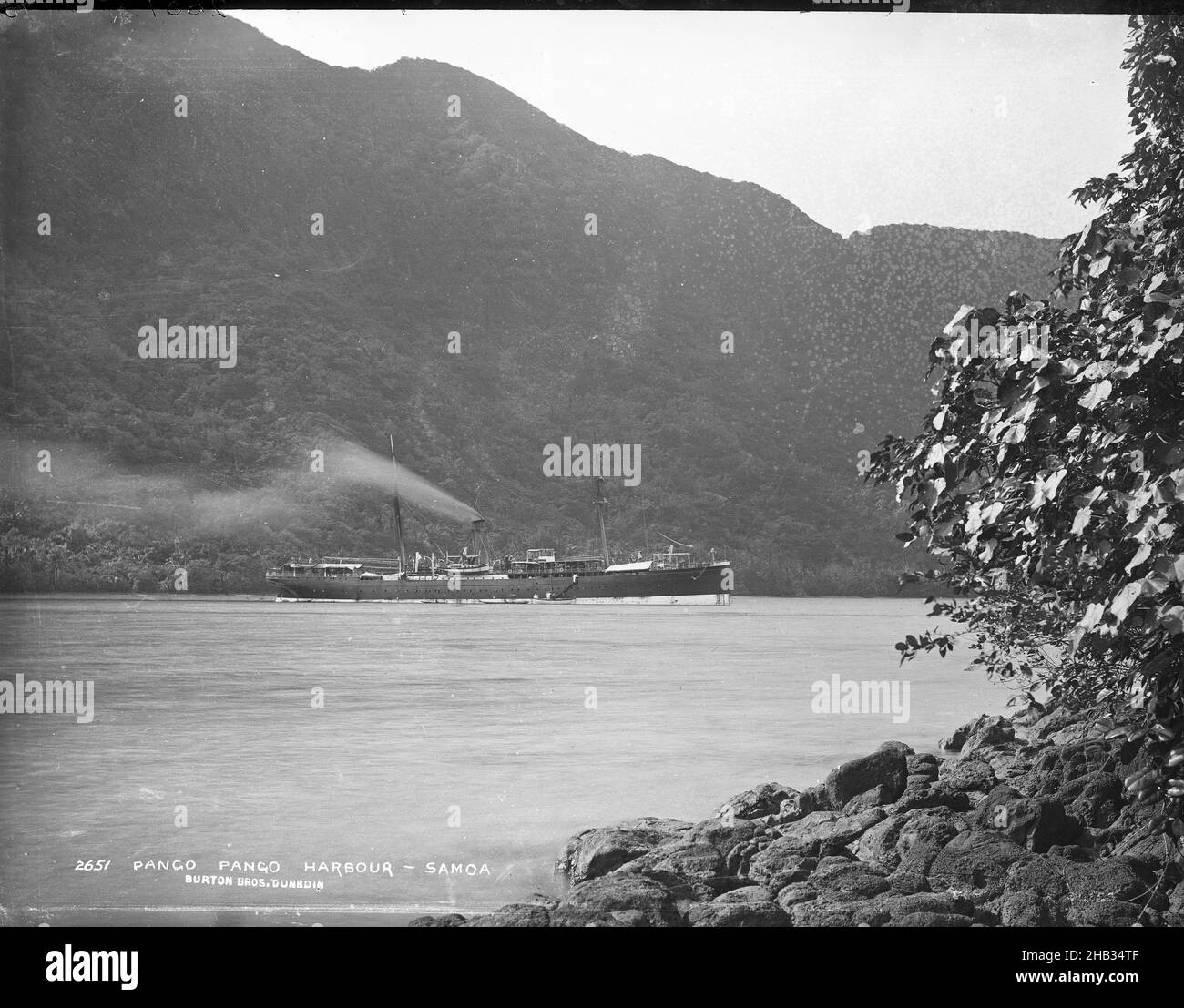 Pango-Pango (sic) Harbour - Samoa, Burton Brothers studio, photography studio, July 1884, Dunedin, black-and-white photography, Rocky foreshore with foliage in right foreground, sea with two masted ship and funnel, smoke drifting from it, facing right. Ladder down on ship with people climbing from longboat. High rising mountain in background. Boat is the 'Wairarapa Stock Photo