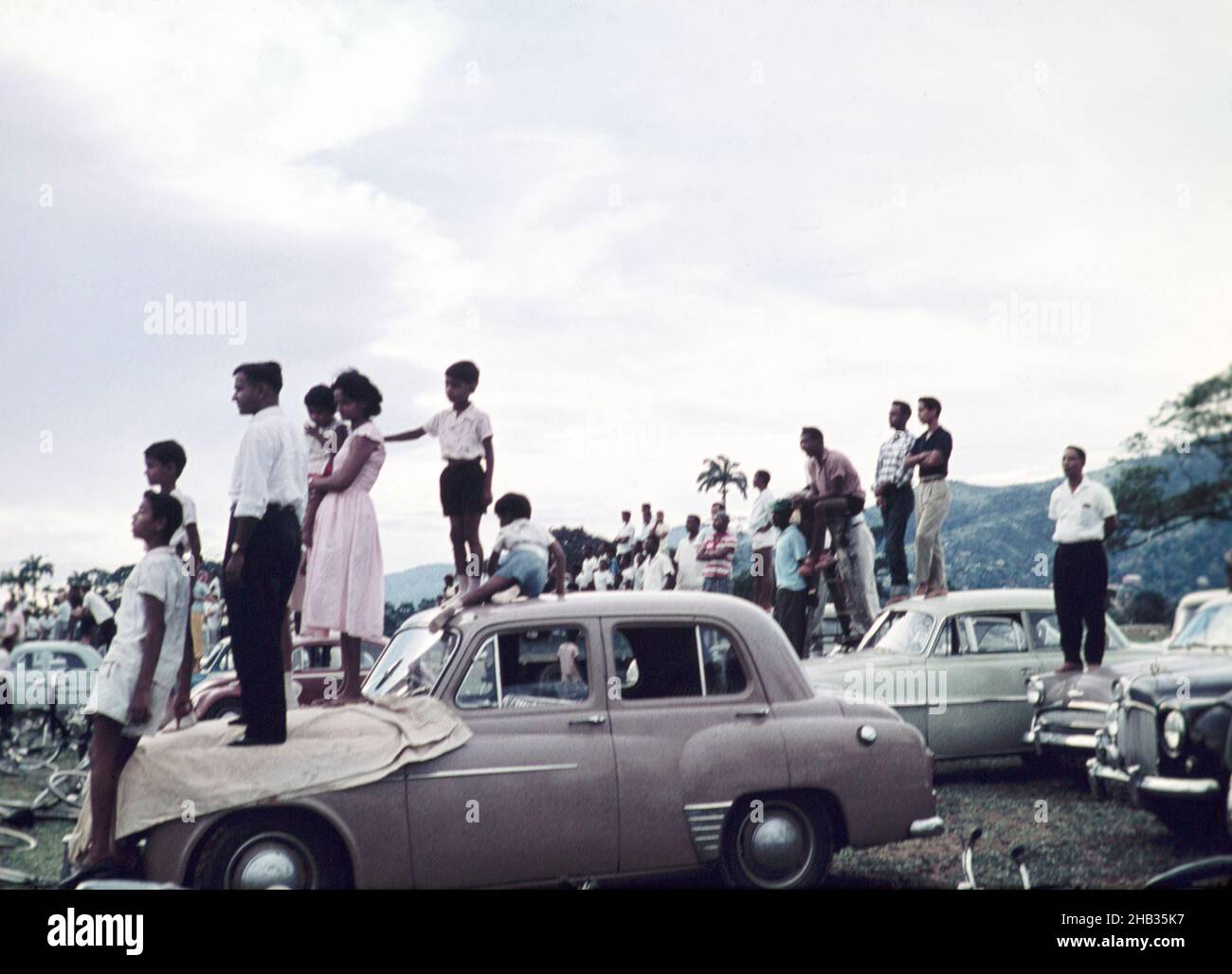 People standing on cars to watch a school sporting event - annual football match between Queen Mary's college and Queen's Royal college - Queen's Park Savannah, Port of Spain, Trinidad c 1962 Stock Photo