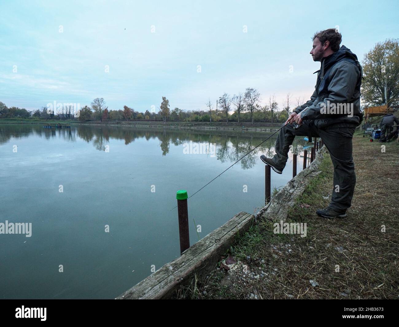 Young Caucasian man catching a fish with a fishing rod at the lake ...