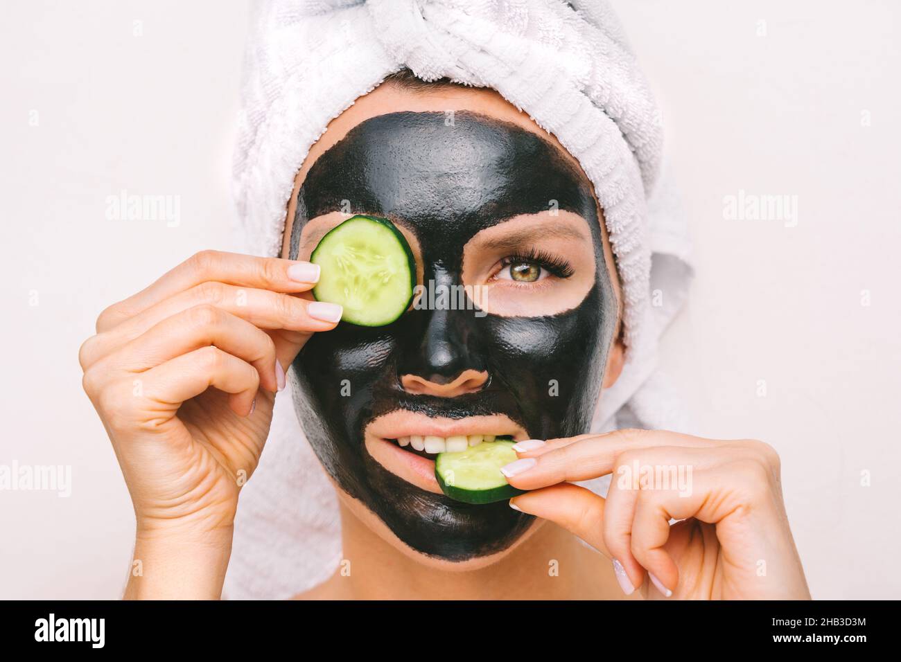 Beautiful woman applying black purifying charcoal facial mask with cucumber slices. Face skin care Stock Photo