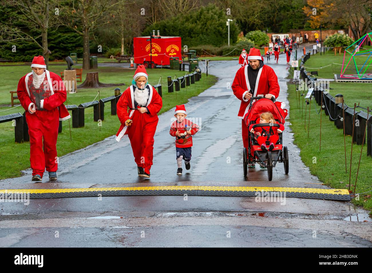 Family of Santa's with child in buggy run up a hill in a Santa Dash Stock Photo