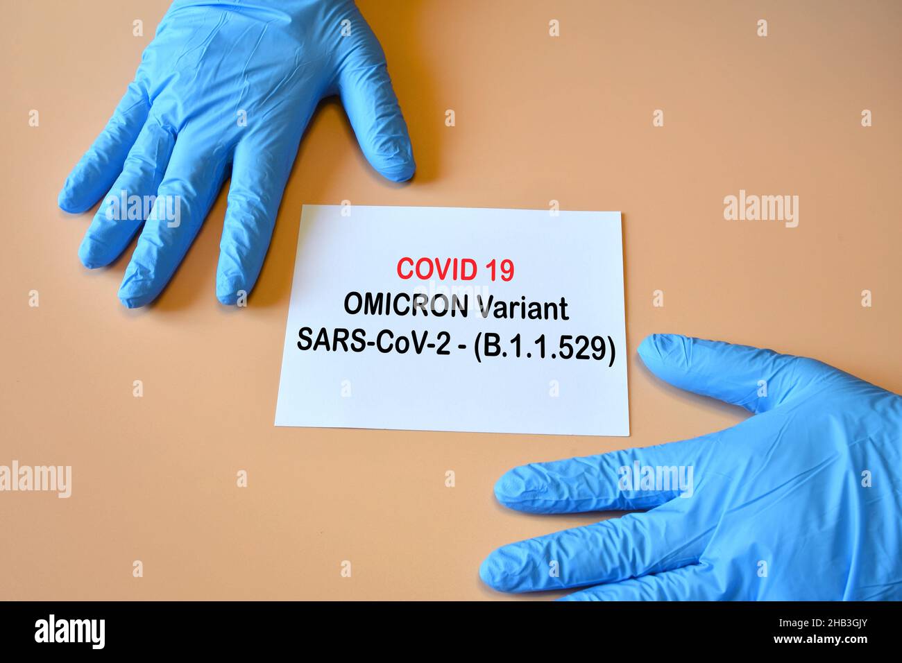 Covid-19 new Omicron variant. Doctor hands with blue gloves and white paper with text 'Covid-19 variant Omicron'. Stock Photo