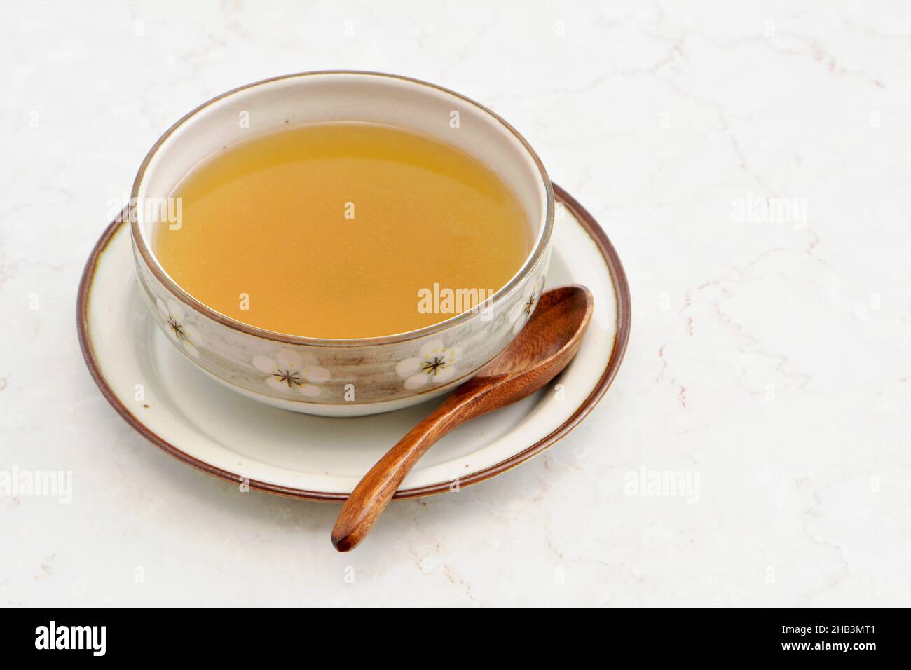 Clear chicken broth soup in pretty chinese bowl with carved wooden spoon on rustic plate. Neutral background with room for text. Horizontal format. Stock Photo