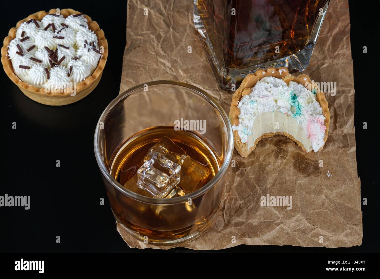 Ice in whiskey glass, surrounded by mini ganache pies and whiskey bottle. Stock Photo