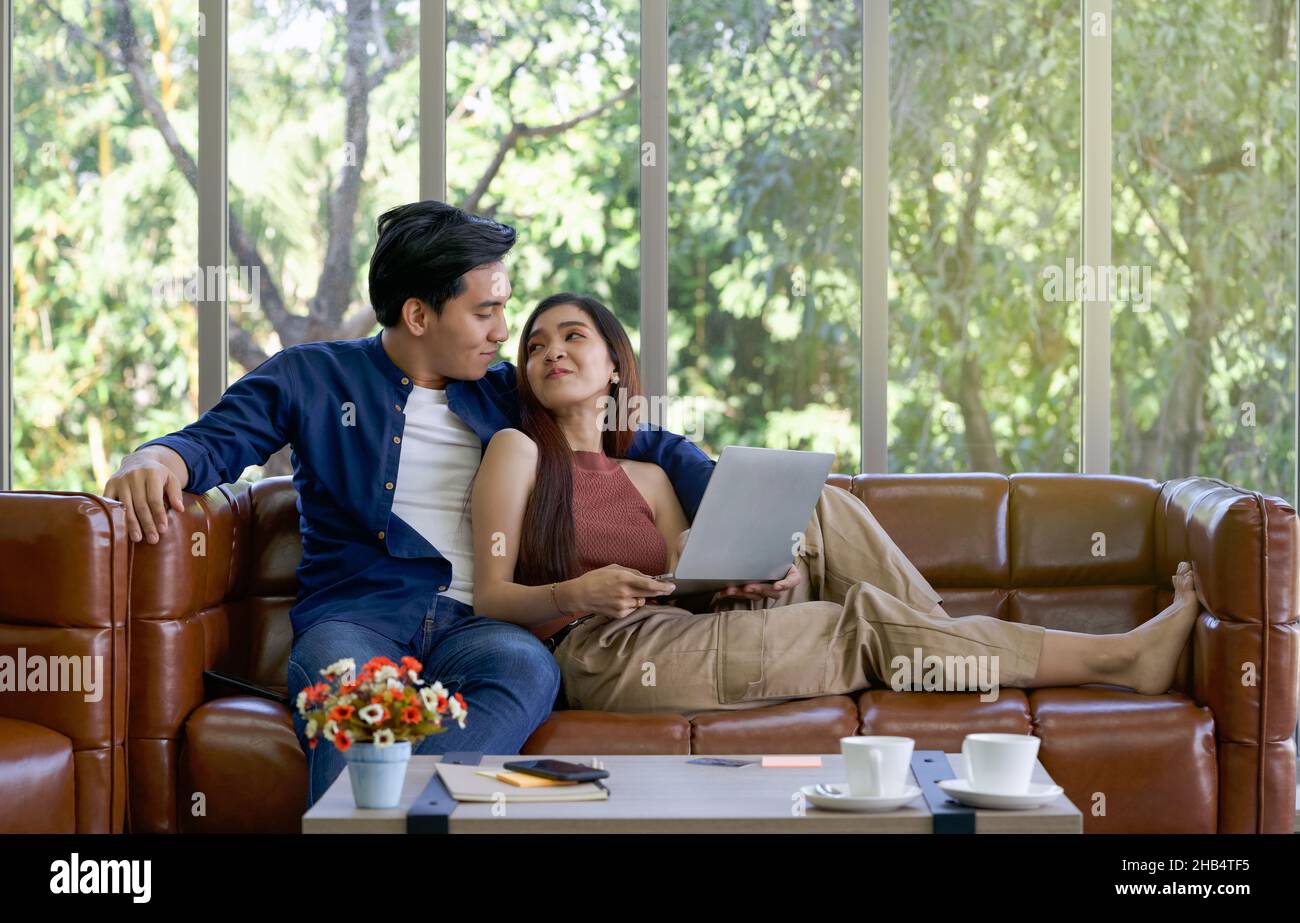 Young lovers spend time together on holidays in the living room. Both make eye contact while the girl held laptop computer. Stock Photo