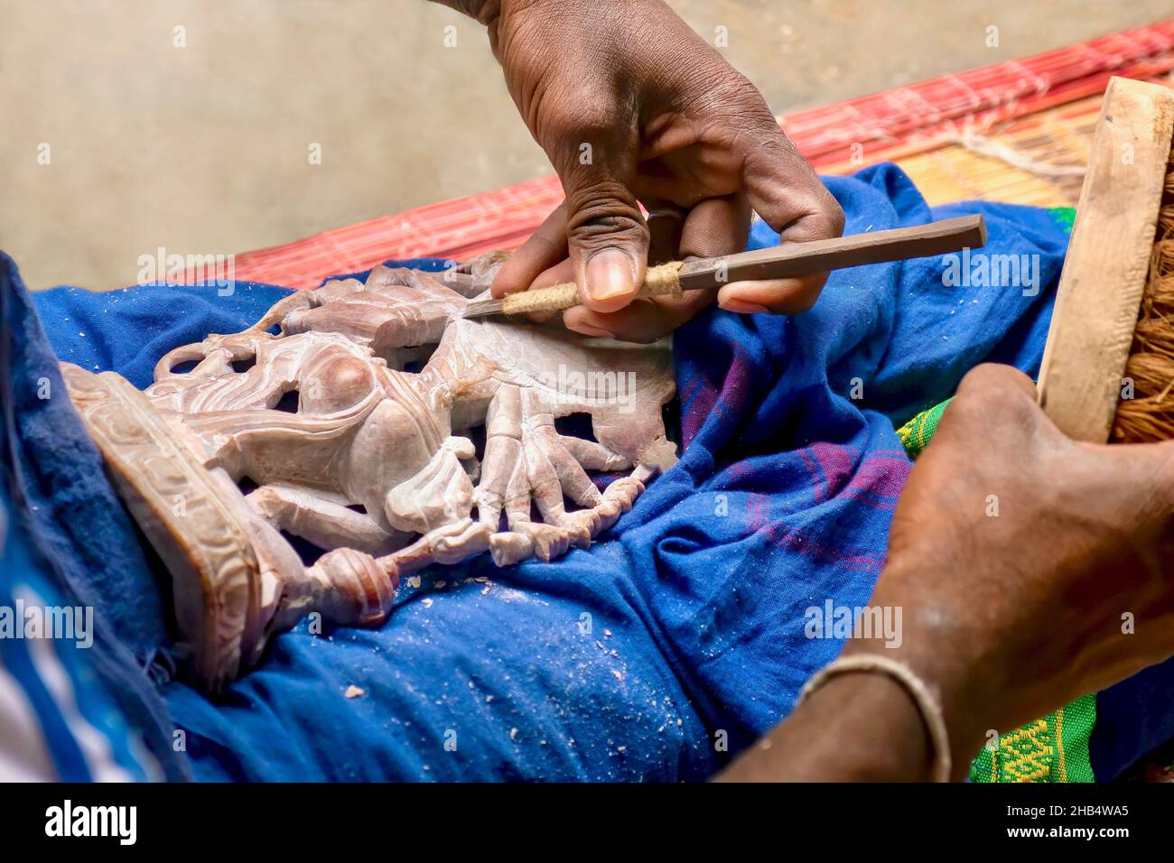 Close-up of a small sandstone religious statue being carved by the hands of a skilled Indian artisan, to sell to tourists as souvenirs, in Tamil Nadu. Stock Photo