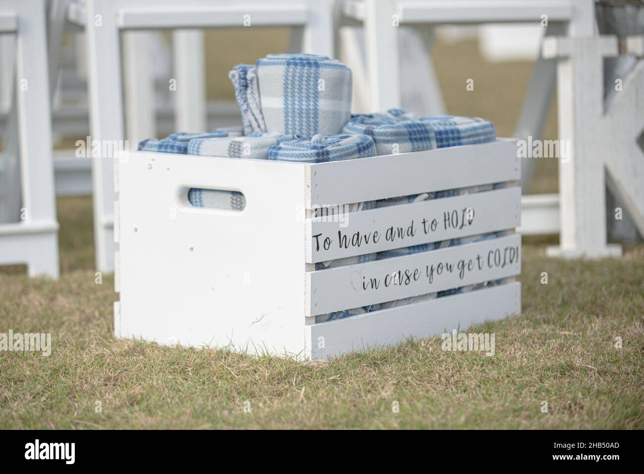 White slated crate at wedding with 'To have and to hold in case you get cold' text containing rolled up guest blankets Stock Photo