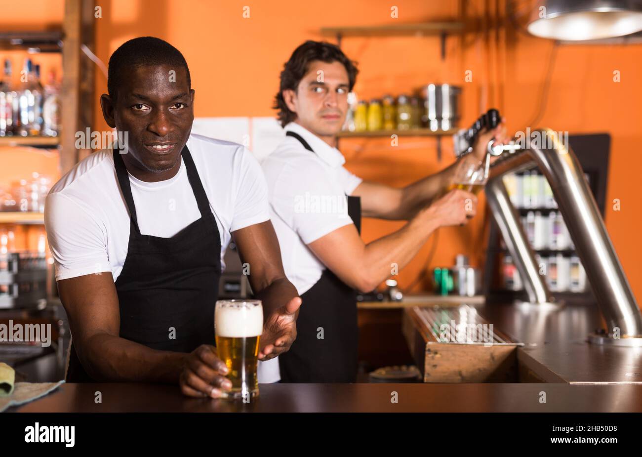 Smiling male bartender wiping a glass and looking away. Barista in