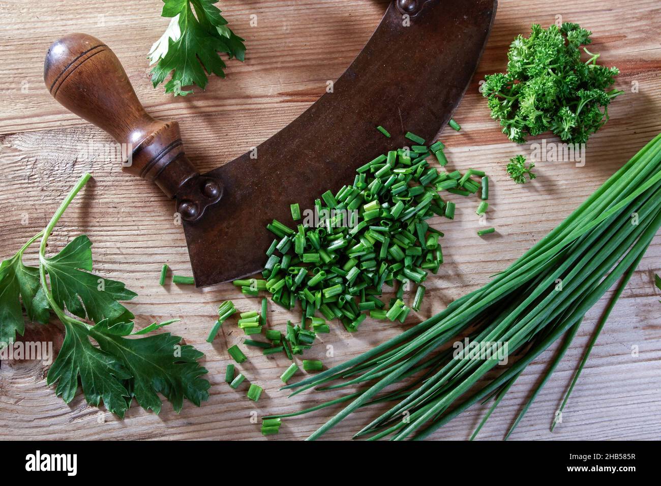 old chopping knife with leek and parsley on a wooden background Stock Photo