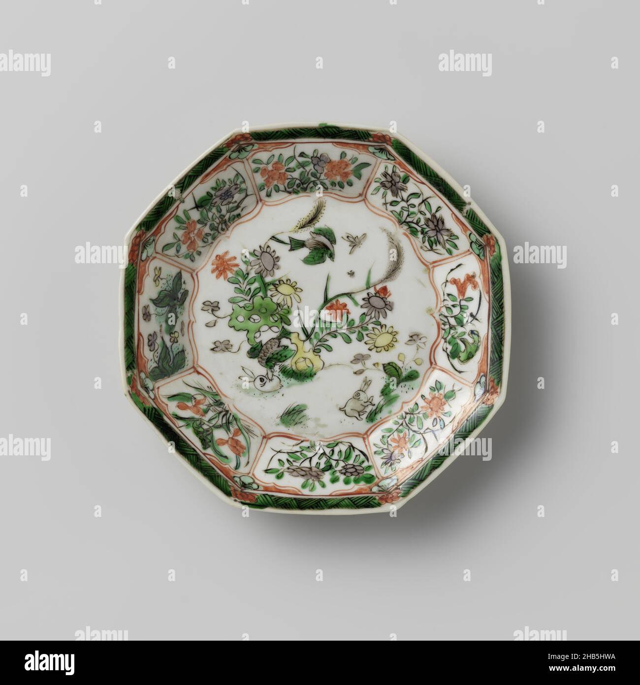 Octagonal saucer with light brown, animals and flower sprays, Octagonal saucer of porcelain, partially covered with café-au-lait, painted in underglaze blue and on the glaze red, green, yellow, eggplant and black. On the flat, two hares and two birds near a rock with flowering plants; the wall with flower branches and butterflies in a box decoration; the rim with zigzag work alternating with flowers. The exterior is covered with a café-au-lait glaze with flower branches. Marked on the underside with a character in a double circle. Famille verte with monochrome brown glaze., anonymous, China, c Stock Photo