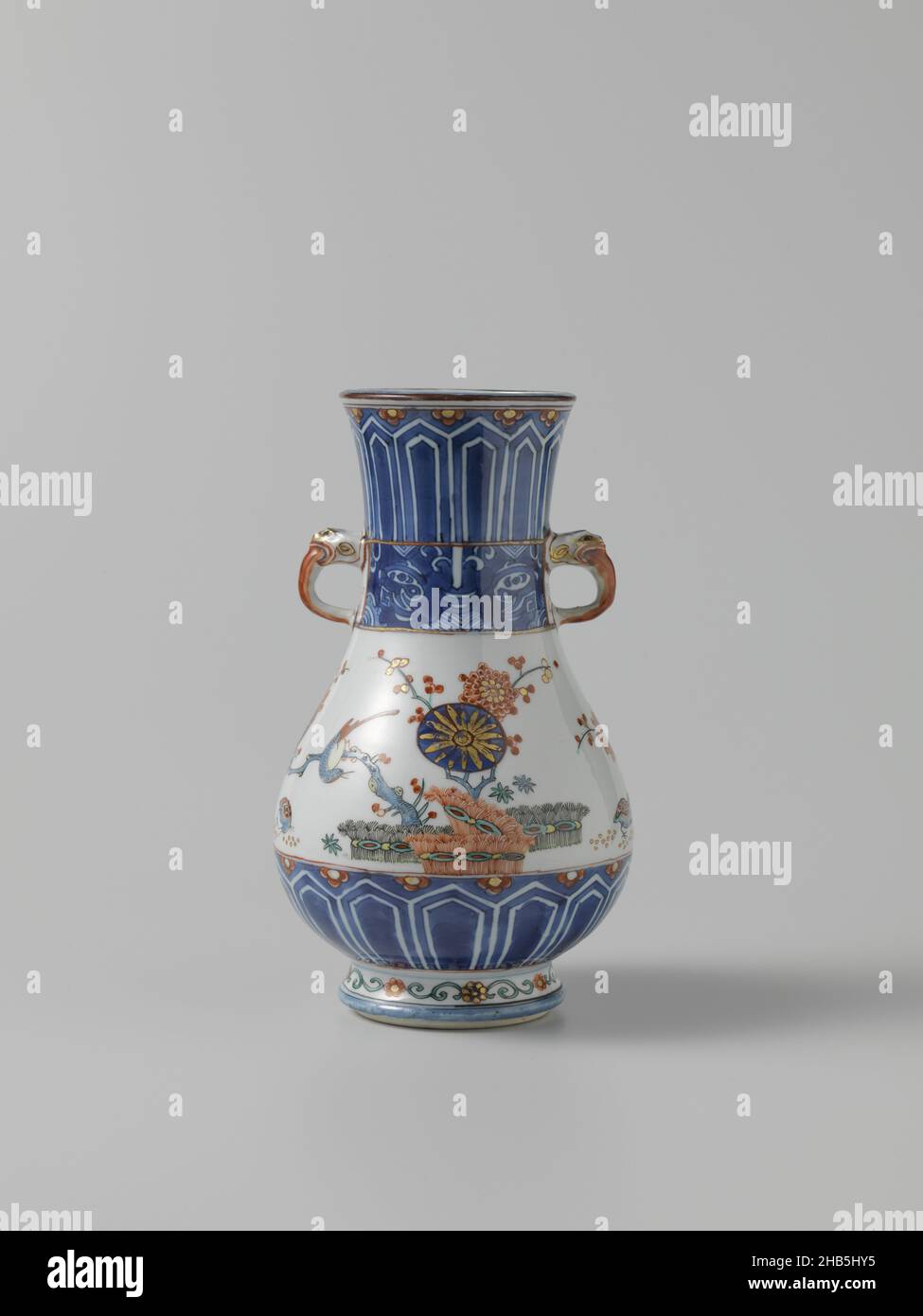 Pear-shaped vase with ornamental borders, flowering plants, brushwood fences and birds, Pear-shaped vase of porcelain with a wide, slightly spreading neck and two modeled ears in the shape of animal heads. Painted in underglaze blue and on the glaze blue, red, green, yellow, black and gold. Decorated in China on the belly in underglaze blue with four yin yang symbols; underneath, a blue band with cut-out leaf motifs and half flowers. The neck with the same band and a band with 'taotie' masks on napkin. In Europe on the belly decorated in enamel colors with birds on prune branches behind tied Stock Photo
