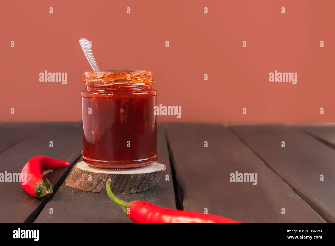 Sweet and spicy red pepper and chili jam in a glass jar on wooden table with copy space Stock Photo