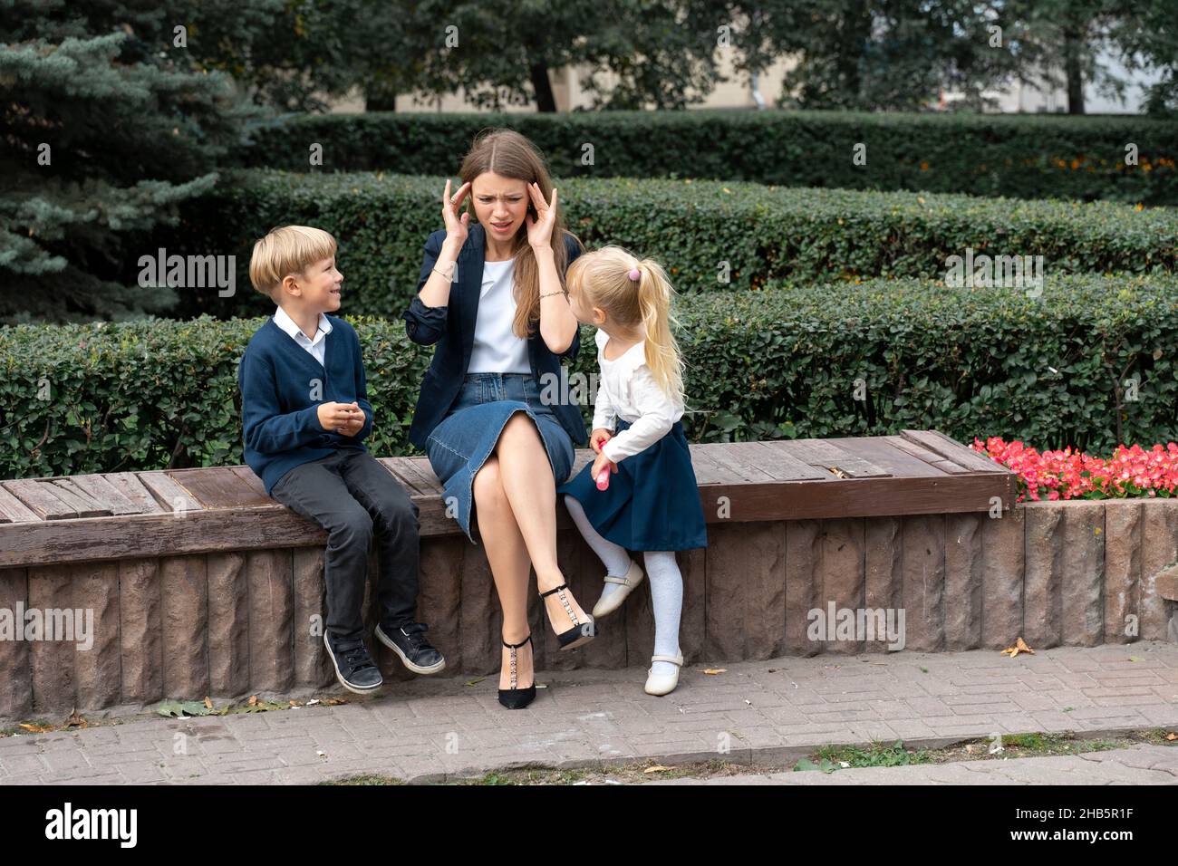 Tired mother having problem with naughty noisy kids, touching forehead, suffering from headache, difficult child, children tantrum and manipulation co Stock Photo