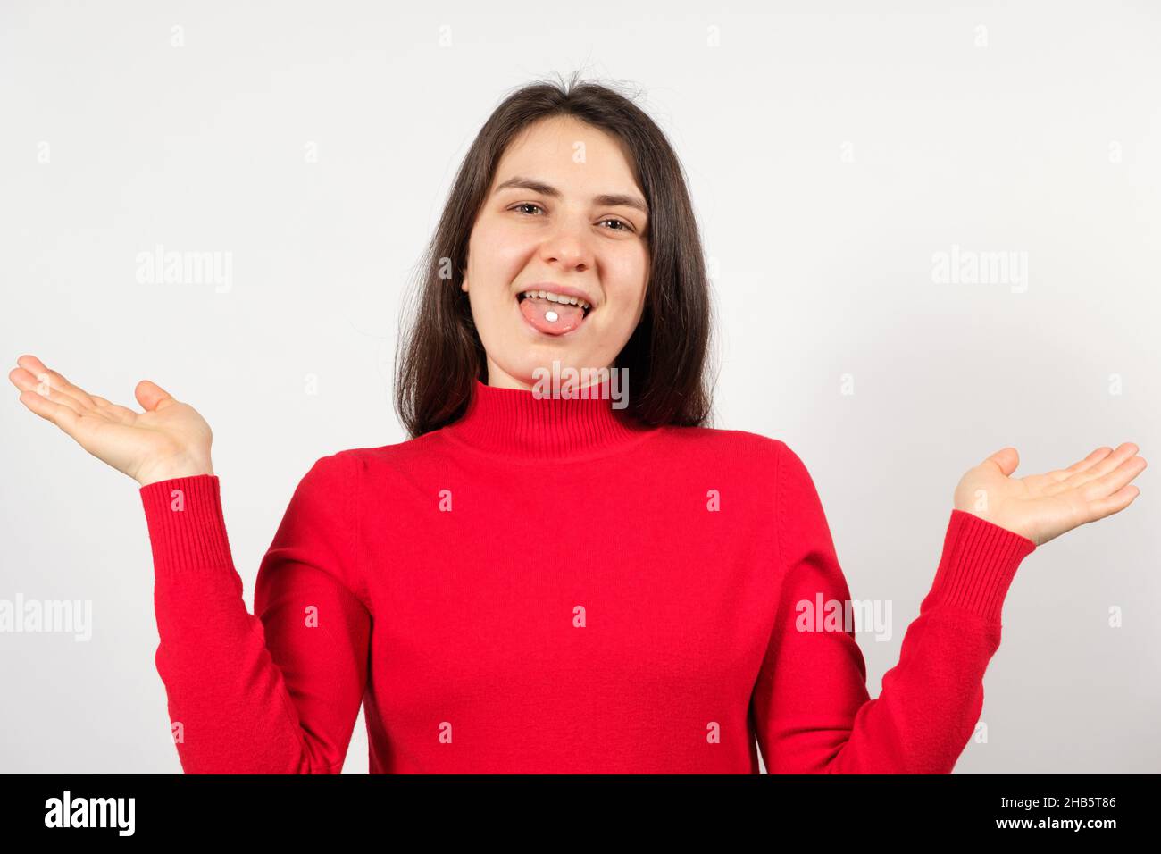 A woman with pills on her tongue spreads her arms apart on a white background. Stock Photo