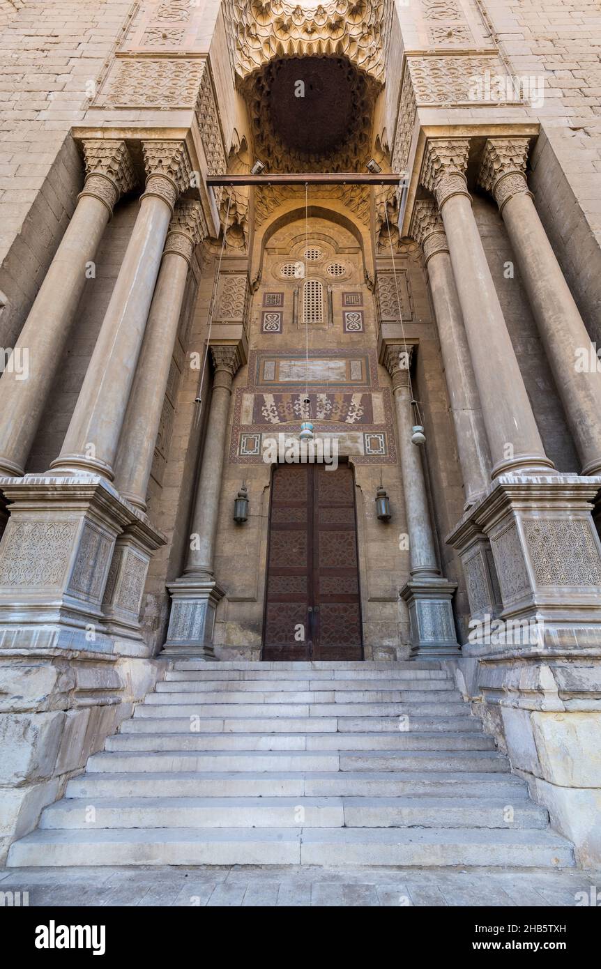 Side gate at al Rifai Mosque, old decorated bricks stone wall with arabesque decorated wooden door framed by marble engraved cylindrical columns, Medieval Cairo Egypt Stock Photo