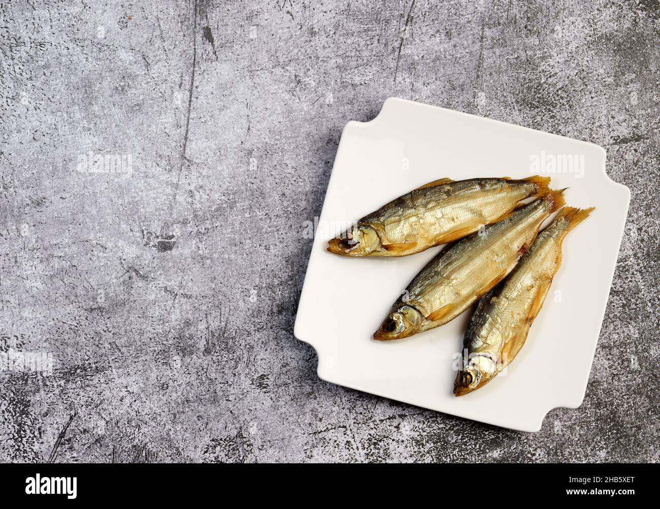 Smoked peled fish (Coregonus peled) on a square plate on a dark background. Top view, flat lay Stock Photo