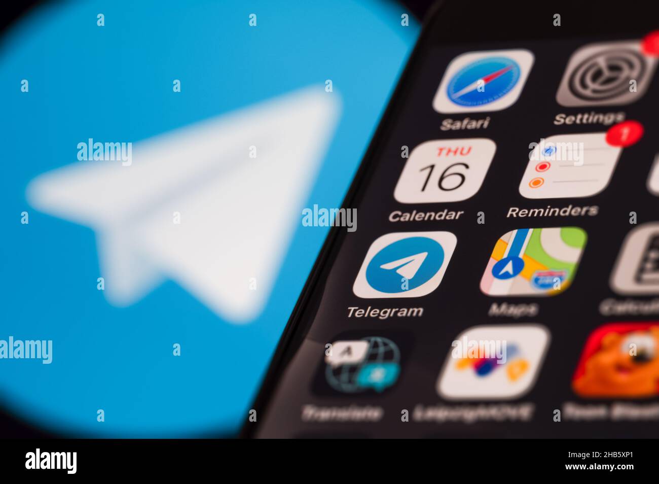 Smartphone screen displaying various application icons. In the background a blurred Telegram logo. Stock Photo