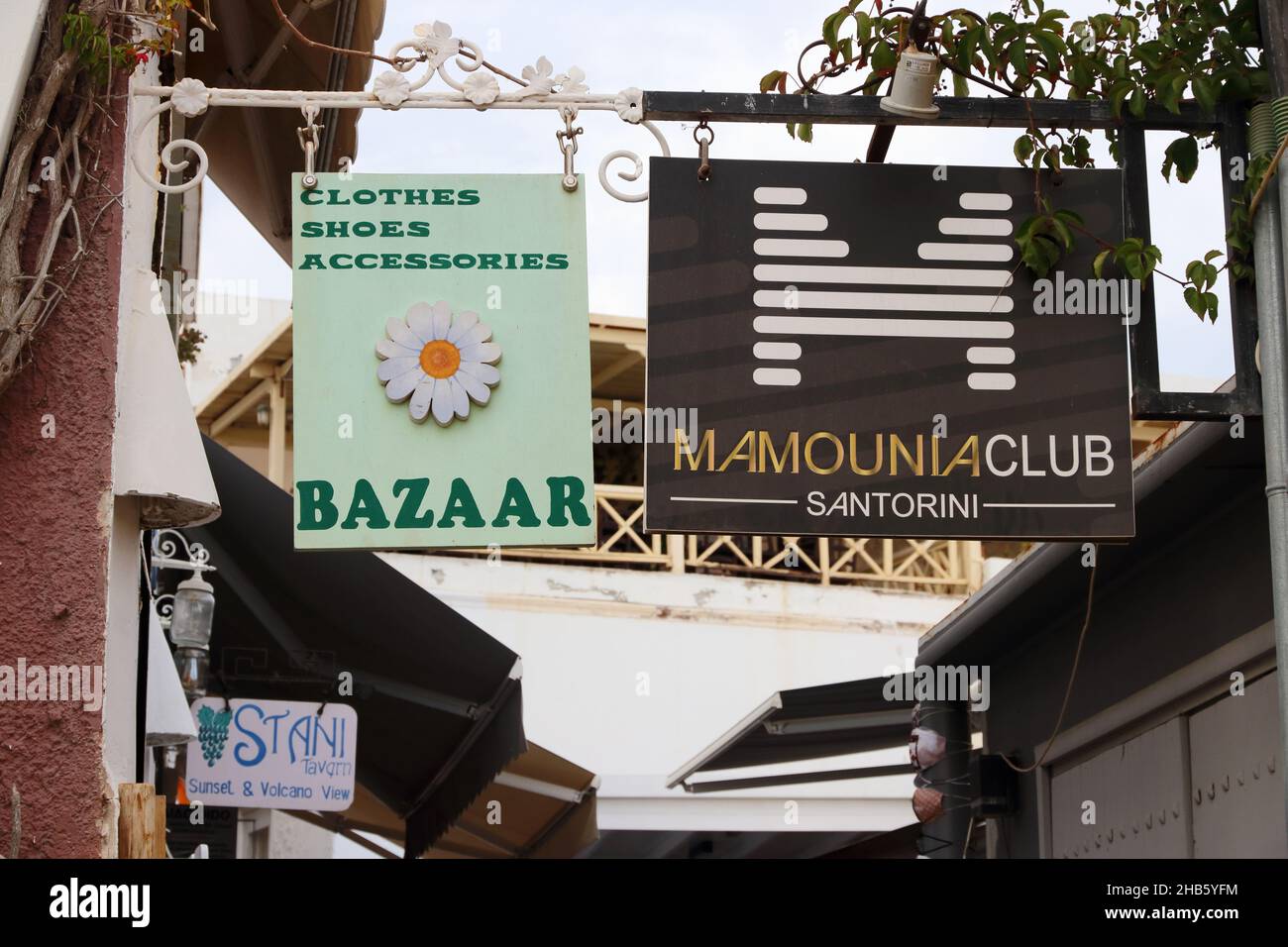 Signs for shops and clubs overhang narrow street, Fira, Santorini, Greece Stock Photo