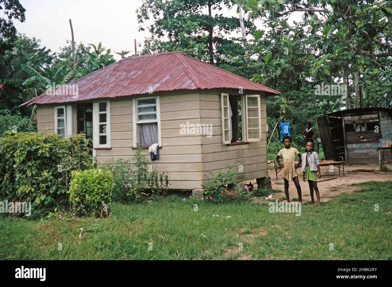 Children standing outside small wooden house, corrugated iron roof ...