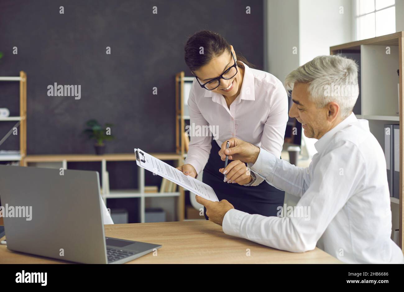 Senior client signs documents at bank agent, financial advisor or insurer's office Stock Photo