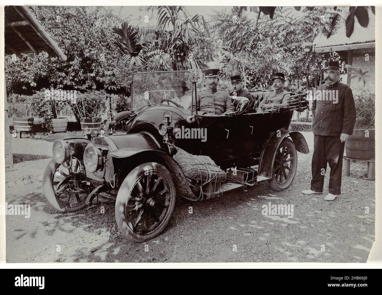 Officers in a car, Number of officers posing in and beside a car with native driver, in a yard in front of house in the bivouac at Krueng Seumpo. Loose photo belonging to an album with 87 photos about the construction of the Gajo road on North Sumatra between Bireuen and Takinguen between 1903-1914., anonymous, Noord-Sumatra, 1903 - 1913, photographic support, width 195 mm × height 135 mm Stock Photo
