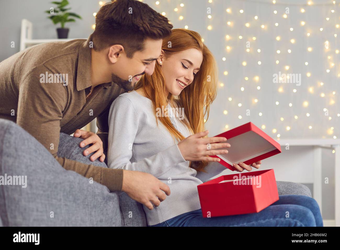 Happy young woman sitting on couch and opening Valentine present from her boyfriend Stock Photo