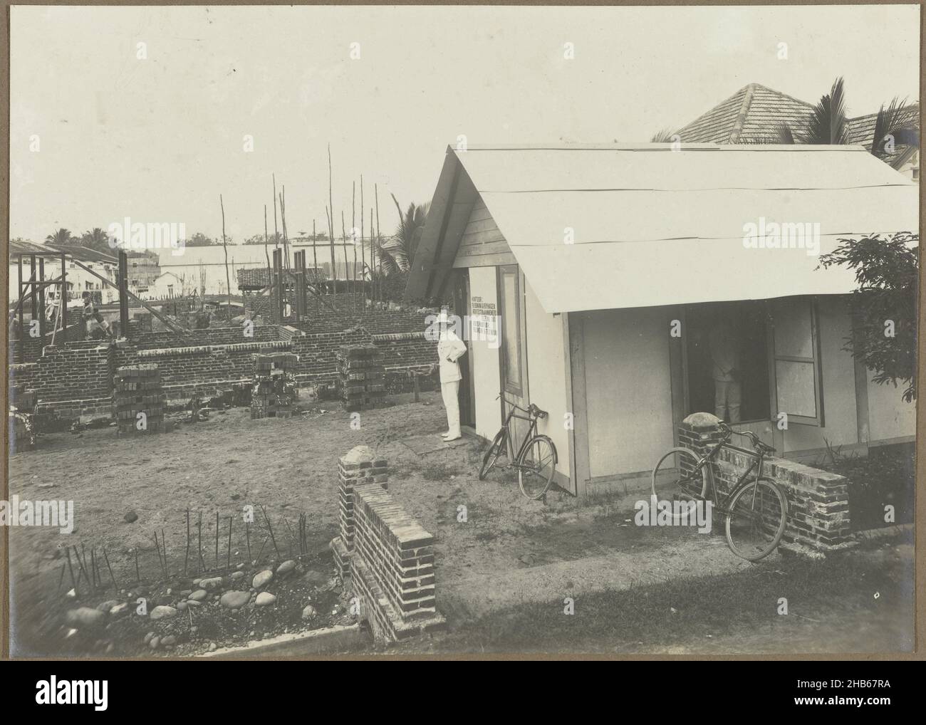 Construction of the Salvation Army Children's Home, The construction of the Salvation Army Children's Home on Wilhelminastraat in Medan in 1916. With Bennink standing in front of the construction company's office on the building site. Photo in the photo album of the Dutch architectural and construction company Bennink and Riphagen in Medan in the years ca. 1914-1919., anonymous, Medan, 1916, photographic support, gelatin silver print, height 145 mm × width 201 mm Stock Photo