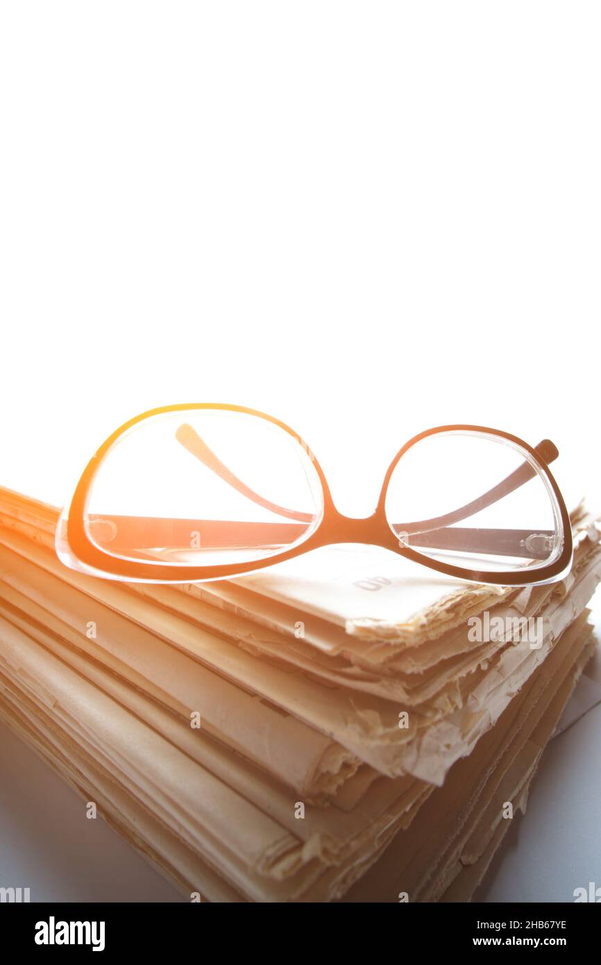 Stack old newspapers and reading glasses white background on a window on a bright sunny day Stock Photo