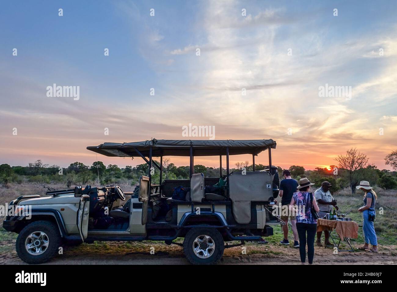 Tourists on a game drive, safari trip, among the wildlife of Kruger National Park, South Africa, having a drink at sunset Stock Photo