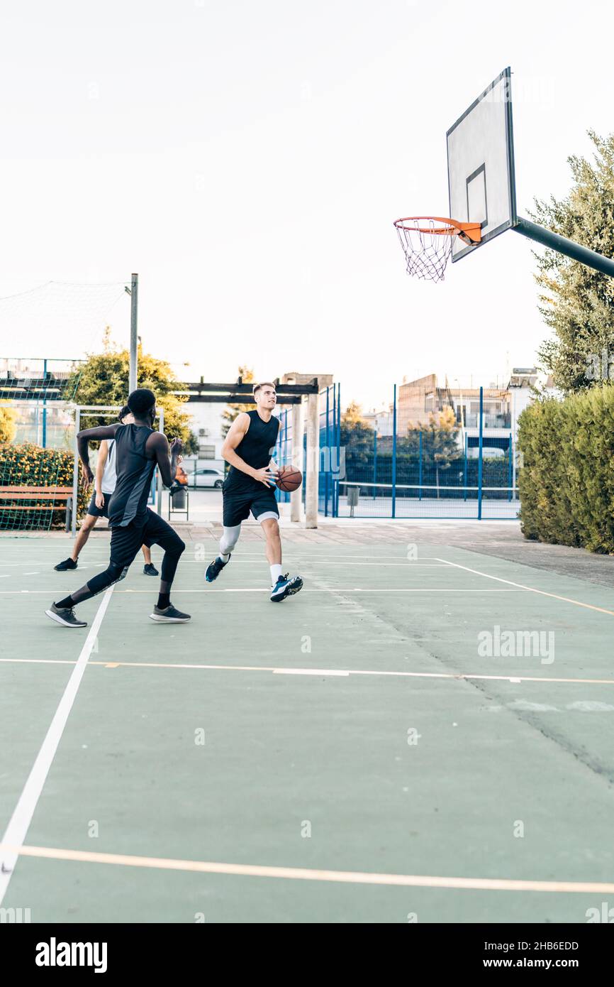 Vertical photo of a group of friends playing basketball in an outdoor space Stock Photo