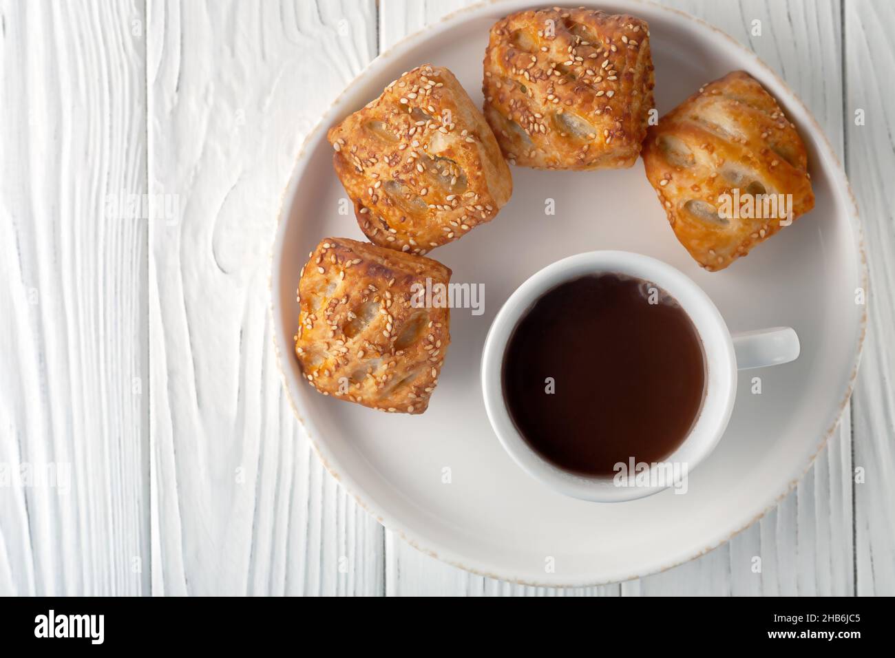 On a white wooden table there is a mug with hot chocolate and fresh aromatic puffs. Stock Photo