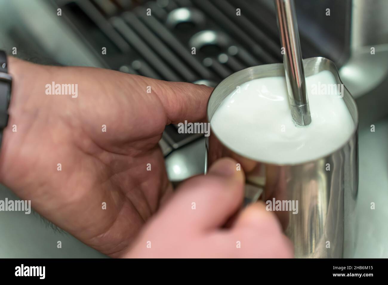 A man whisks milk for a latte in a steel jug. Stock Photo