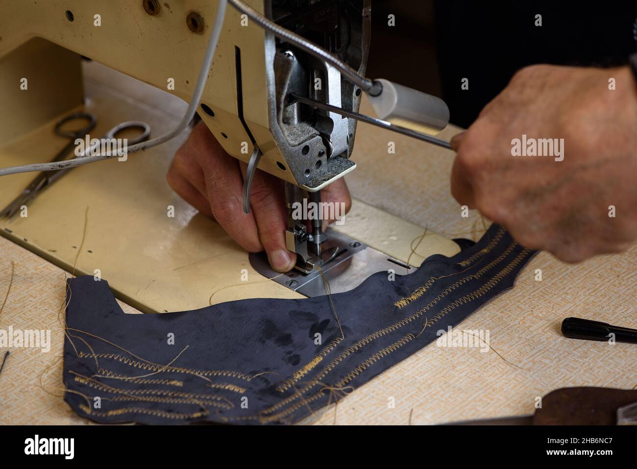 Mechanic repairing industrial sewing machine in factory. Hands of