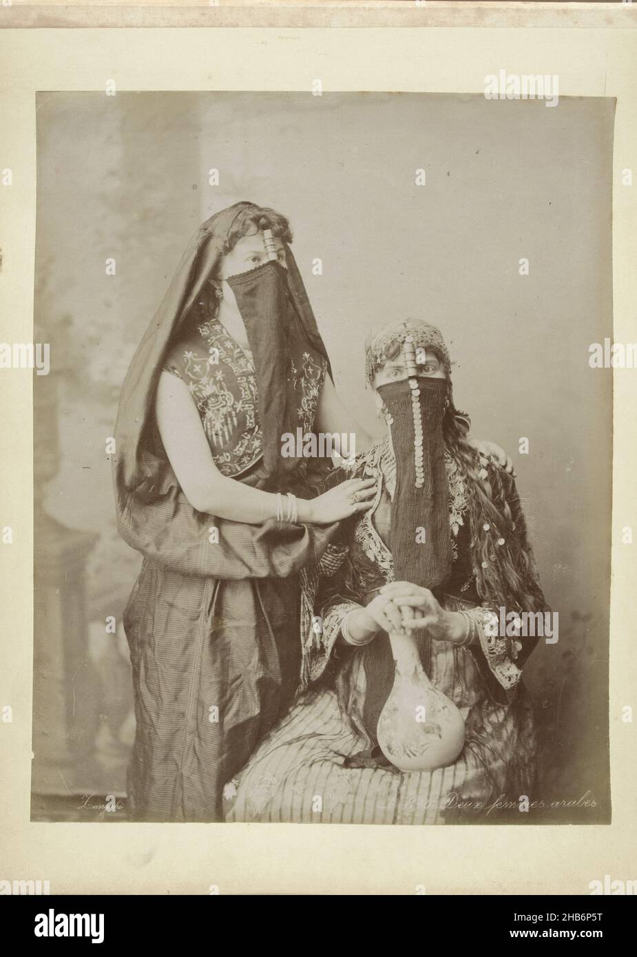 Portrait of two veiled women, No 810. Deux femmes arabes (title on object), They carry in front of face, from top of nose, a cloth, on lap one of them has an earthenware jug, Zangaki (mentioned on object), Egypte, c. 1895, photographic support, albumen print, height 277 mm × width 216 mmheight 277 mm × width 367 mm Stock Photo