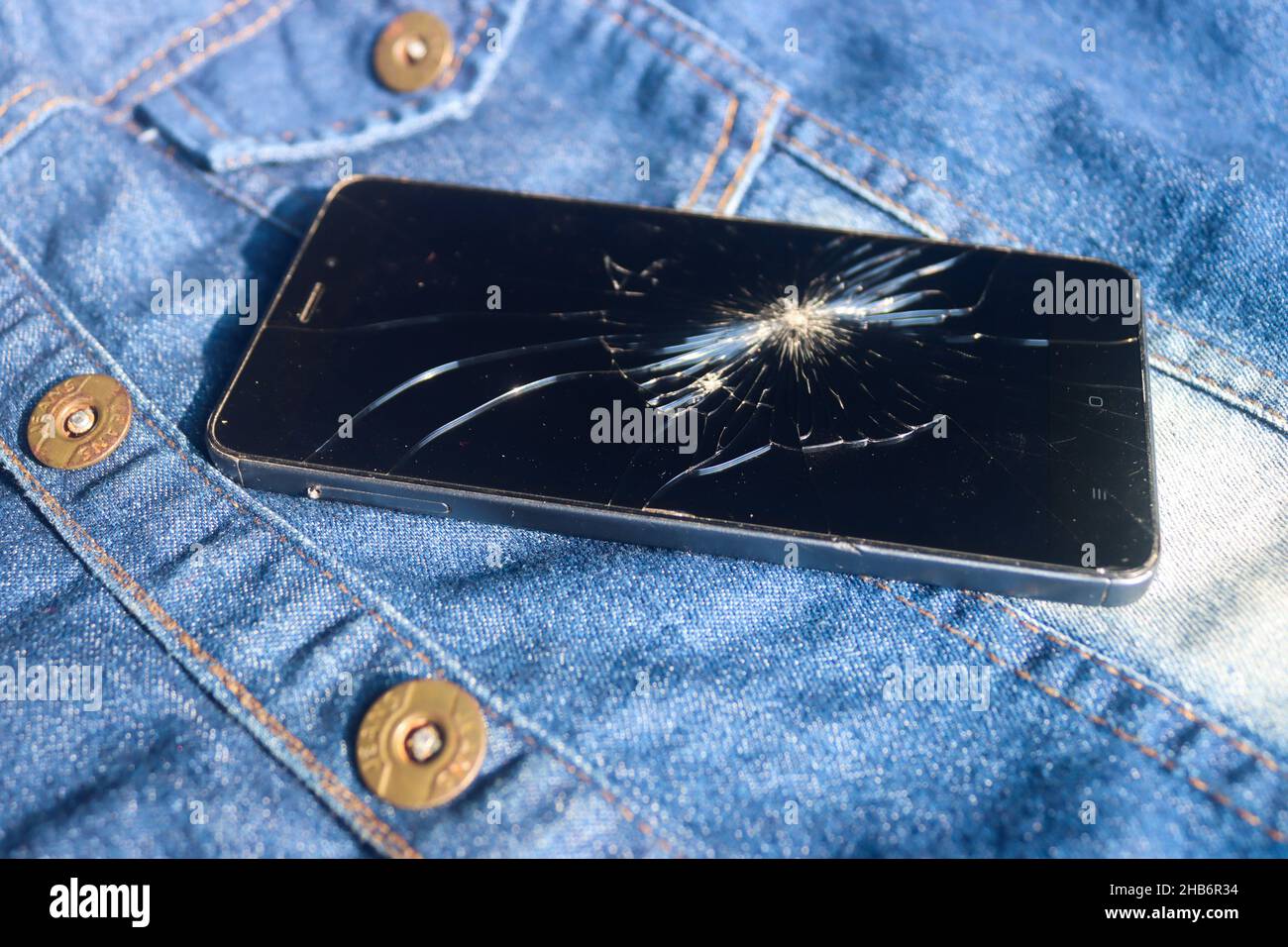 Broken mobile broken cell phone placed on dennim jacket Stock Photo