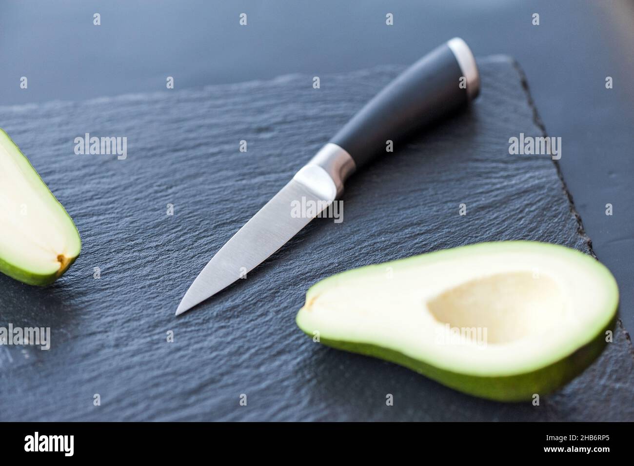 Male hands about to slice the freshly avocado with a chefs kitchen knife on a matte black