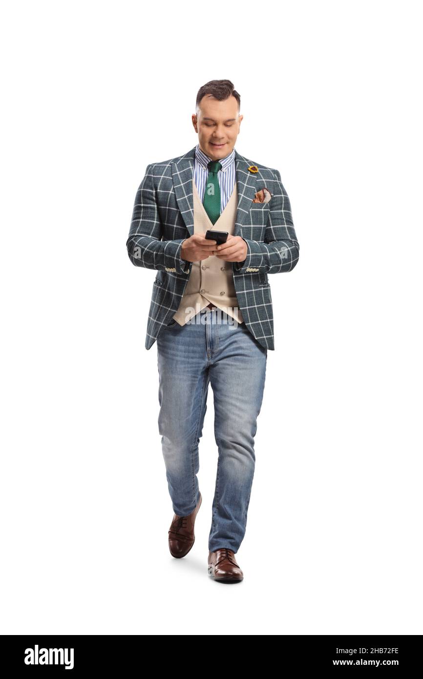 Full length portrait of a man in stylish suit and jeans walking and using a smartphone isolated on white background Stock Photo