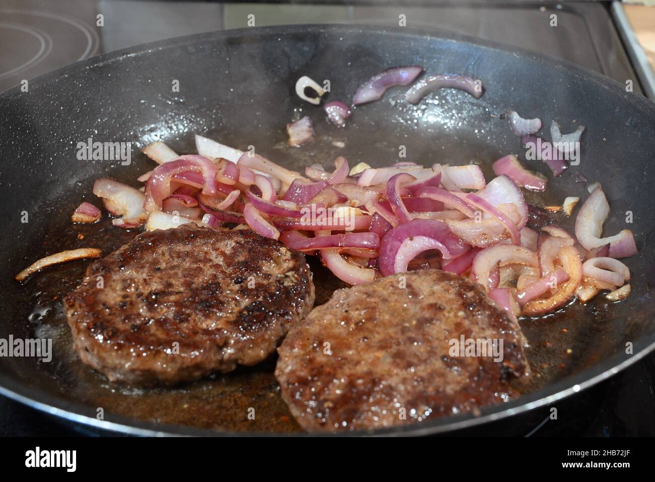 beef burgers and red onions frying in a pan Stock Photo Alamy