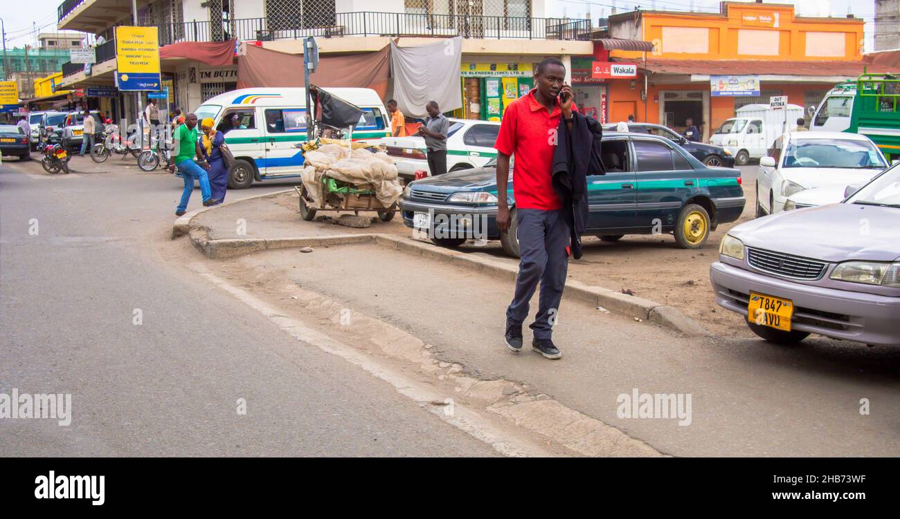 ARUSHA, TANZANIA - MARCH 16, 2017: Pedestrian on a cell phone with a background of pedestrians and retail stores in Arusha, Tanzania Stock Photo