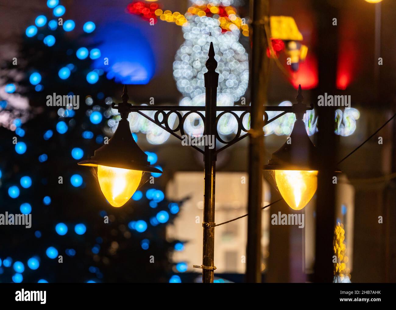 Vintage retro style double high street shopping lights. Lamps with Christmas decorations illuminated and snowman lit up behind out of focus. Stock Photo