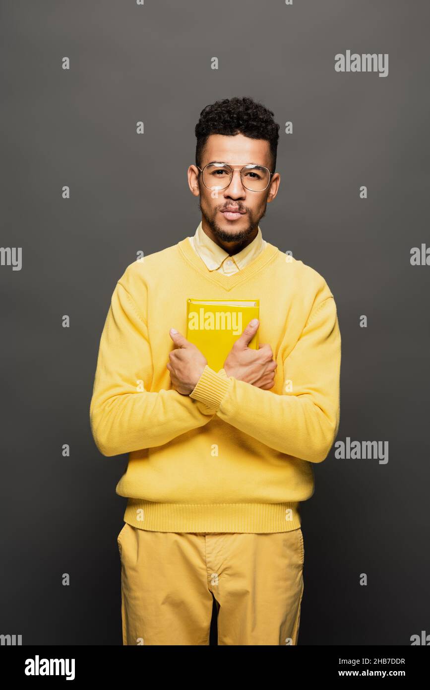 curly african american man in glasses and yellow outfit holding book on ...