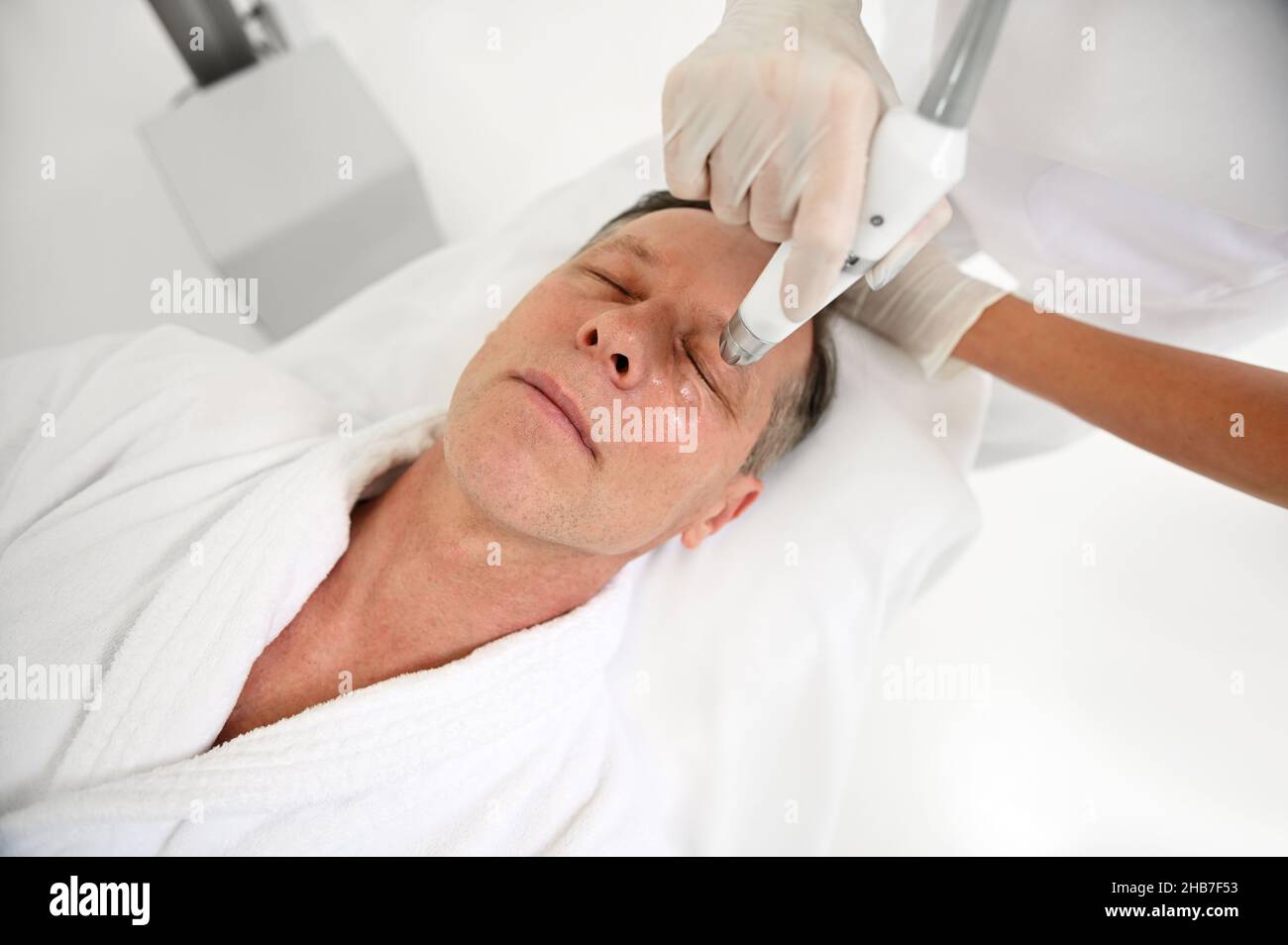 Rejuvenating facial treatment. Overhead view of mature man getting lifting therapy massage in wellness SPA clinic. Exfoliation, stimulation and hydrat Stock Photo