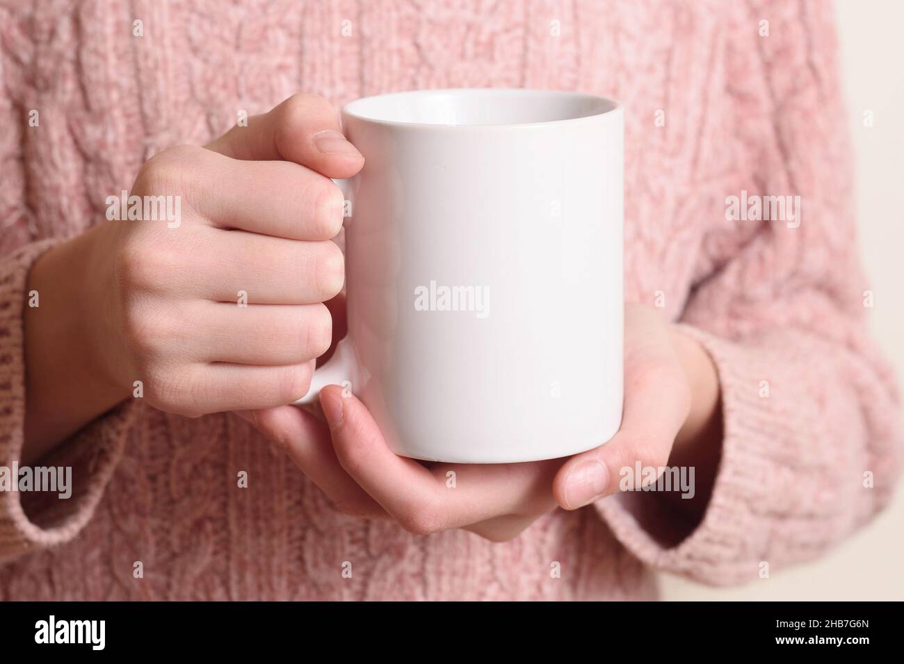 Young woman in warm sweater is holding white mug in hands  Stock Photo