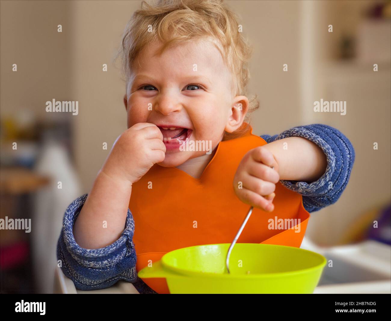 Happy one year old baby boy smiling eating with cutlery at home Stock Photo