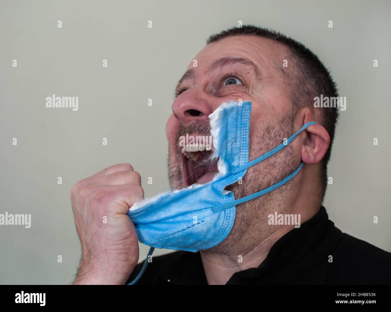 Close-up of a man tired of wearing the mask.  Gone mad, he snatches it Stock Photo