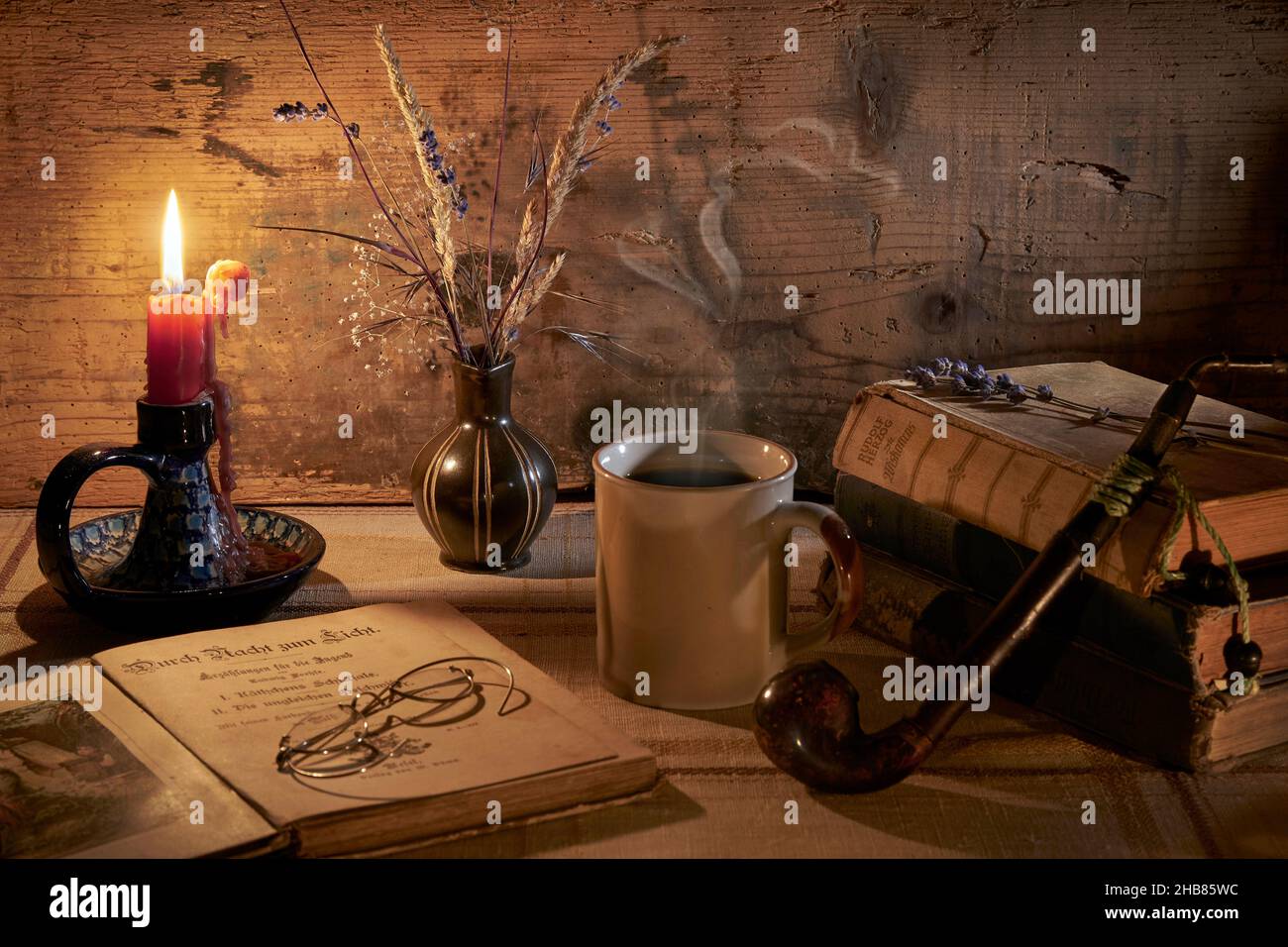 Retro Stillleben mit dampfender Kaffeetasse, Büchern, Tabakpfeife, alte Brille, Kerzenhalter mit tropfender Kerze, Vase mit Gräsern und Lavendel Stock Photo