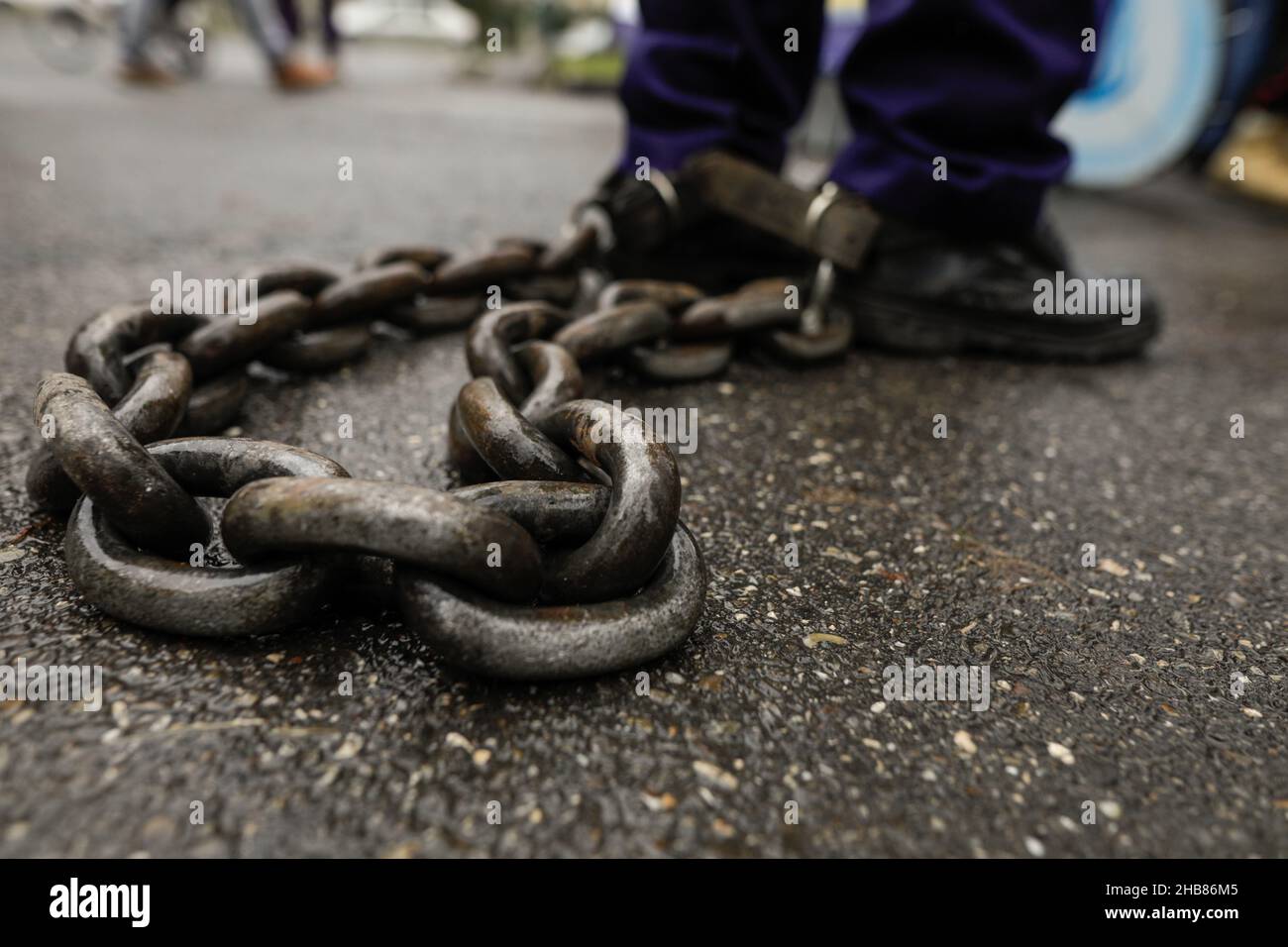 Shallow depth of field (selective focus) details with a rusty metal chain tied to a man’s feet. Stock Photo