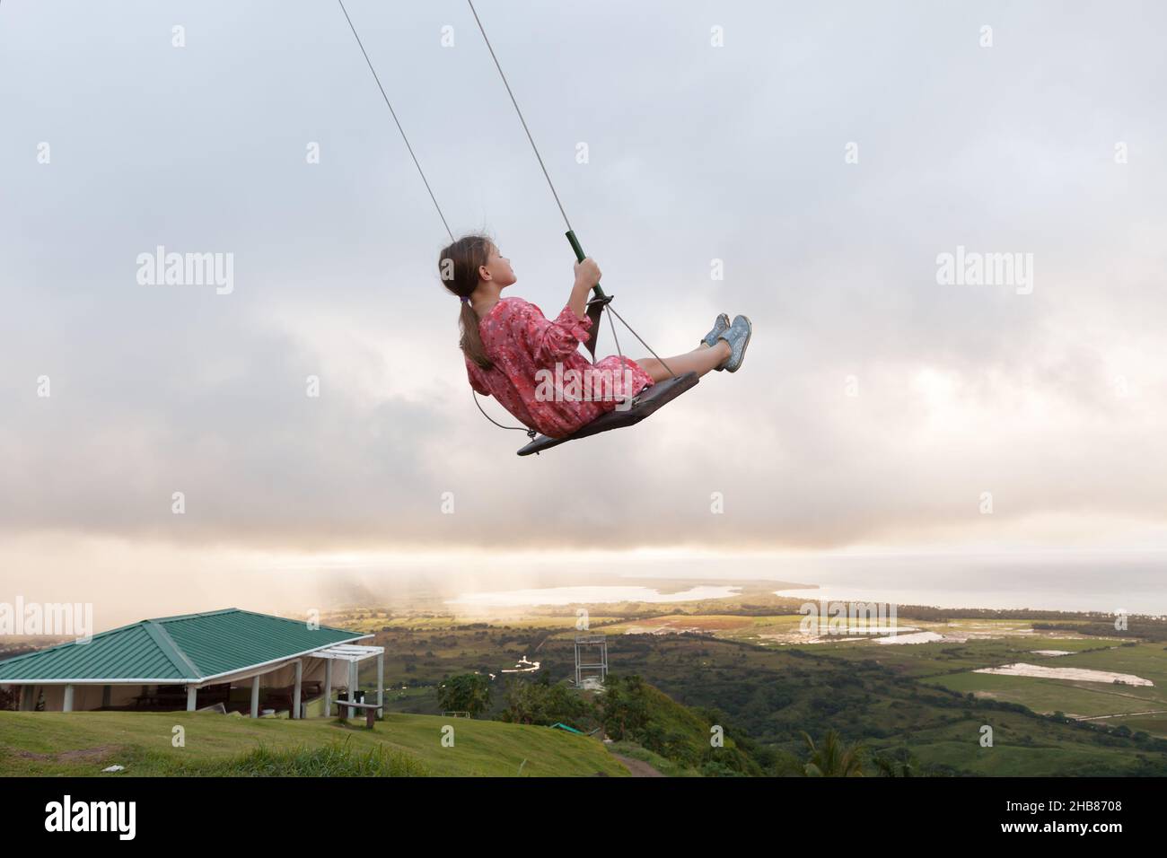 Little girl is on a swing under cloudy morning sky at the top of the mountain Montana Redonda in Dominican Republic Stock Photo